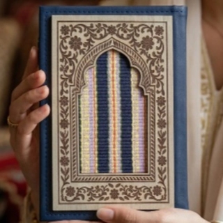 A navy leather notebook decorated with wood and hand-woven Sadu embroidery.