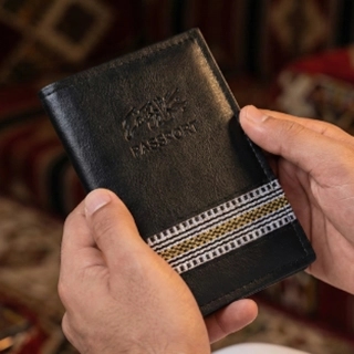 A luxurious black passport cover made from recycled leather, adorned with hand-crafted gold and silver Sadu weaving.